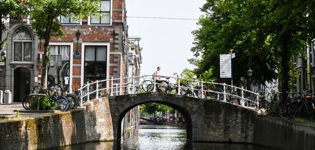 Vrouw die over een brug fiets bij een gracht in Delft