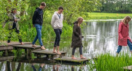 Groep mensen loopt op blote voeten over het blotevoetenpad bij De Boerinn in Kamerik, omgeven door groen en water in het Groene Hart.