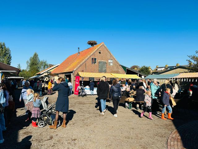 Bezoekers genieten van de Goede Doelen Dag in Zegveld met marktkraampjes bij een boerderij onder een blauwe lucht.