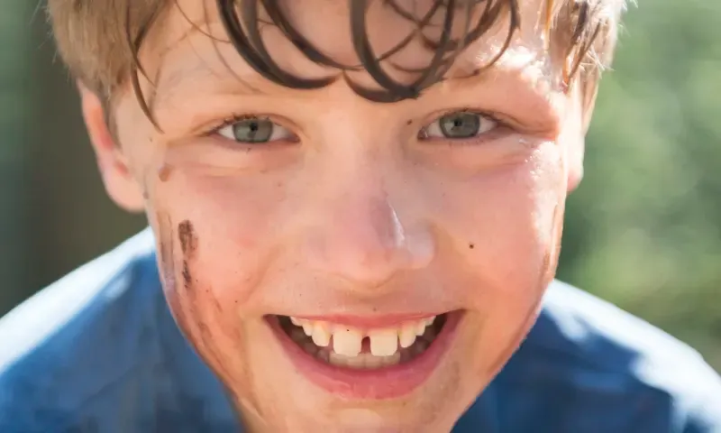 Lachende jongen die in de modder heeft gelegen.