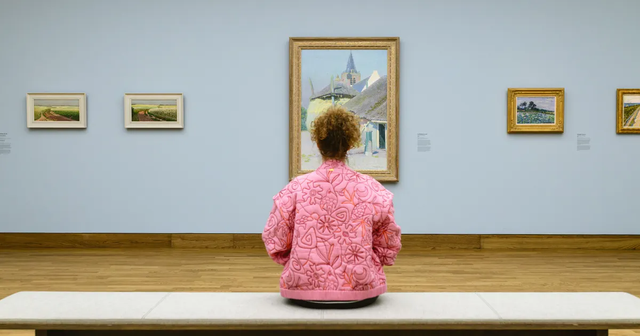 Bezoeker in Singer Laren kijkt naar kunstwerk terwijl ze op een bankje zit.