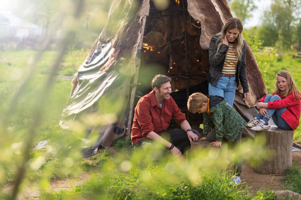 Een gezin met twee kinderen zit voor een hut in het hunebedcentrum.
