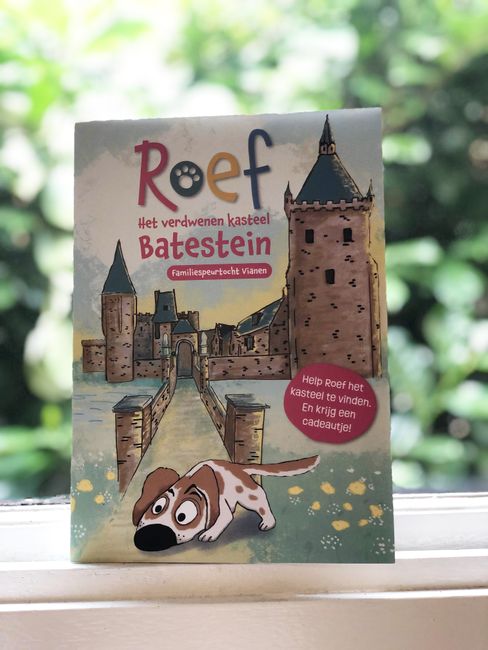 Een foto van een folder met daarop een cartoon van hondje Roef die voor een kasteel in het gras staat.
