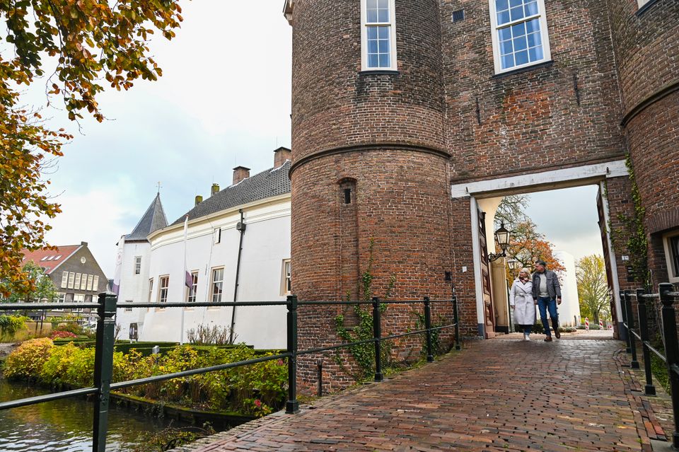 Wandelaars lopen door de poort van Kasteel Montfoort, naast de oude stadsmuur en de gracht. De historische binnenstad en het water bij de Hollandse IJssel geven een sfeervol beeld van de middeleeuwse vestingstad Montfoort.