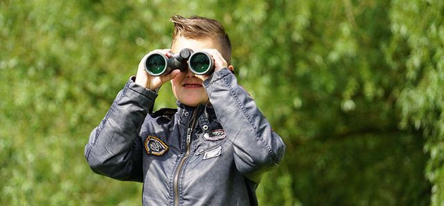 Een kind die door een verrekijker kijkt in de bossen