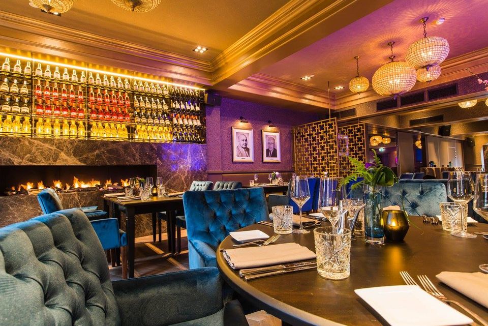 Sfeervol interieur van restaurant De Heeren van Montfoort met luxe tafels, fluwelen stoelen, warme verlichting en een uitgebreide wijnwand op de achtergrond.