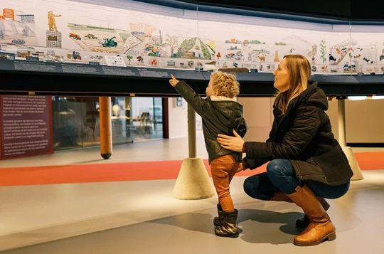 Een moeder en kind bekijken de geborduurde wandpanelen van Museum Batavialand