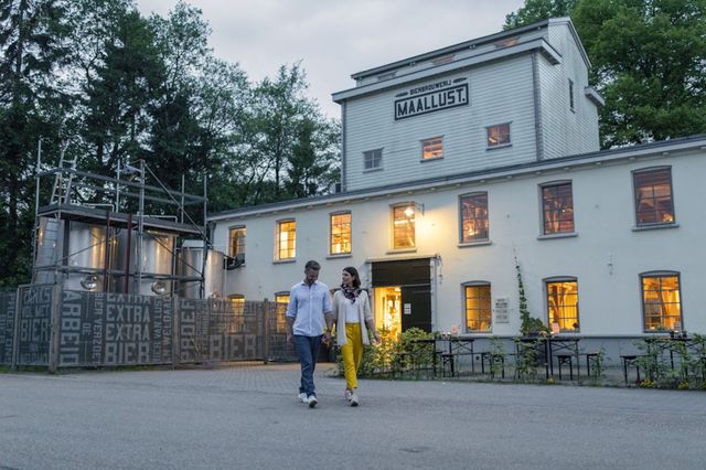 Ein Paar läuft vor dem weißen Gebäude der Bierbrauerei Maallust in Veenhuizen vorbei.
