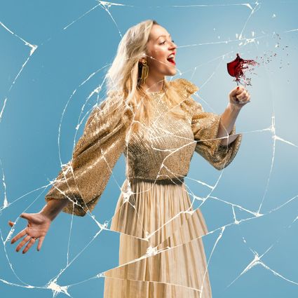 Céline Jansen in een goudkleurige kleding. Zij zingt en breekt daardoor een glas.