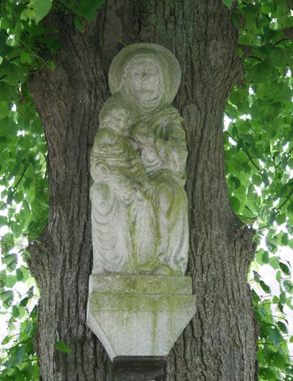 beeld van Maria met kind hangend tegen een boomstam net onder het gebladerte