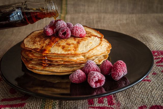 Op een bord ligt een stapel pannenkoeken met frambozen en stroop.