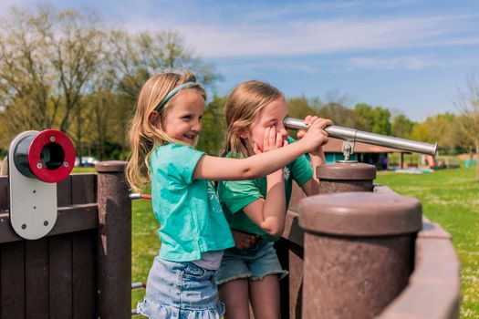 Meisjes kijken door een verrekijker op een speeltoestel.