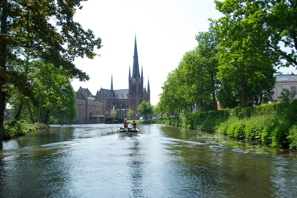 Mensen varen met een sloep over de singel van Woerden met op de achtergrond de Bonaventurakerk en zomers groen aan de waterkant