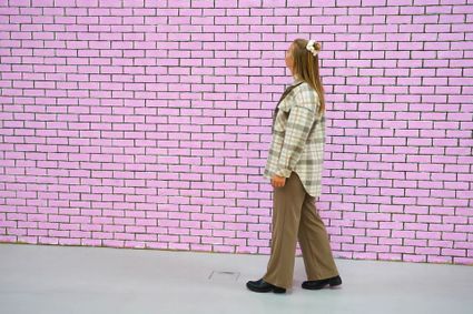 Een muur met roze beschilderde bakstenen waar een jonge dame voorstaat en naar kijkt.