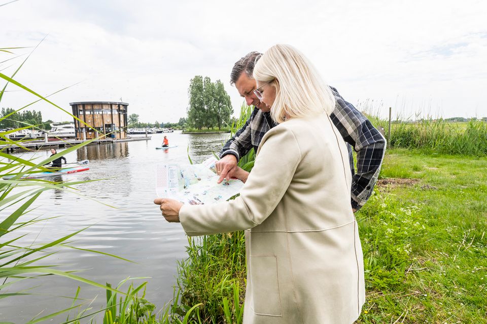 Jachthaven Marnemoende in IJsselstein, Groene Hart. Wandelaars bekijken een routekaart aan de waterkant, met de jachthaven, recreatieboten, suppers en het Hollandse IJsselpad in het groene polderlandschap.