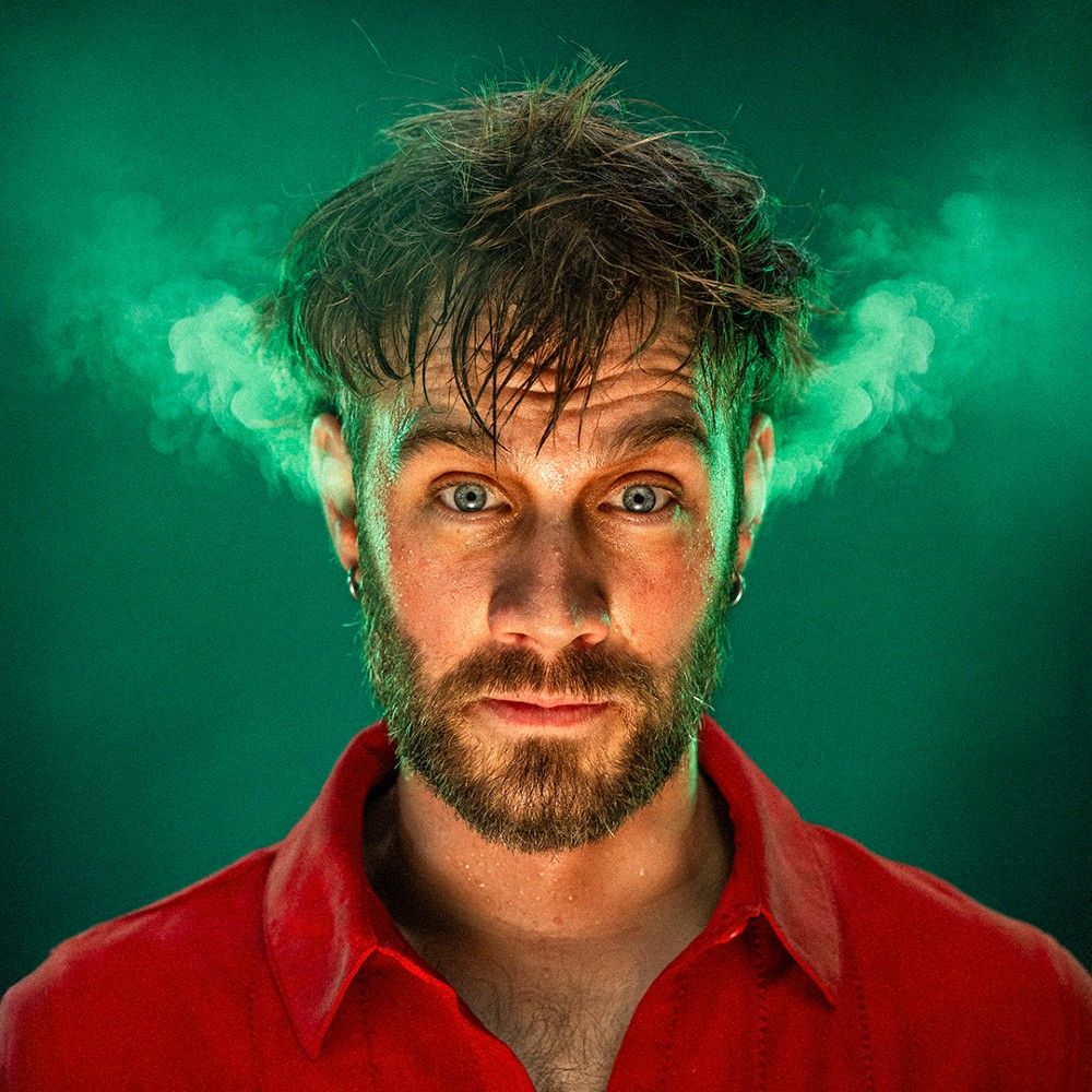 Foto van Pieter met rood overhemd aan, tegen een groene achtergrond. Er komt "stoom" uit zijn oren.