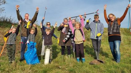 Kinderen en volwassen met attributen voor opruimen in de natuur op een rijtje in het gras.