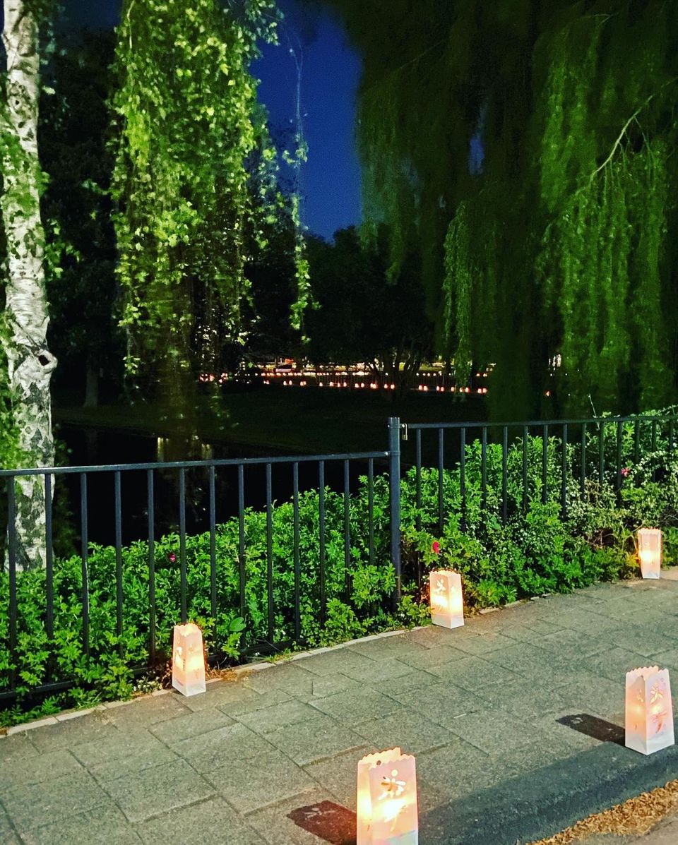 Lichtzakken langs een wandelpad bij water en bomen tijdens de 24 Uur van Woerden, met sfeervolle verlichting in een groene, natuurlijke omgeving in de avond.