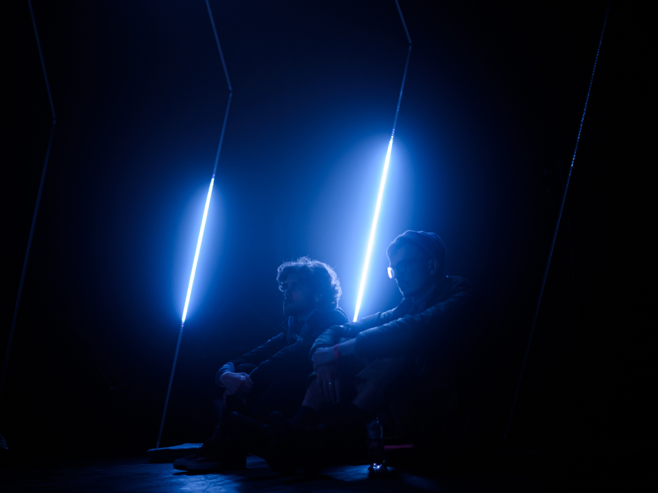 Twee mannen die op de vloer zitten met blauwe lichtstralen achter hen tijdens Highlight Delft, een lichtfestival in Delft