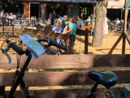 Fiets met fietsroute op houder met op achtergrond de speeltuin van het Boscafe in Oisterwijk