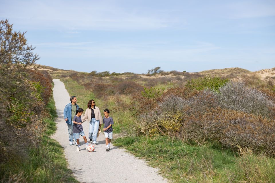 Ouders wandelen met hun twee voetballende zonden door de duinen van Wassenaar.
