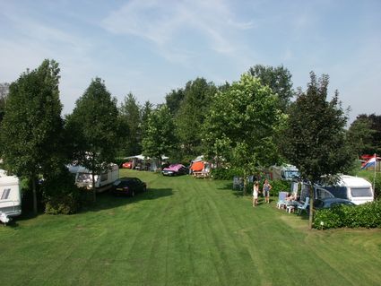 Foto van groot groen grasveld met links en rechts bomen en daaronder verschillende caravans.