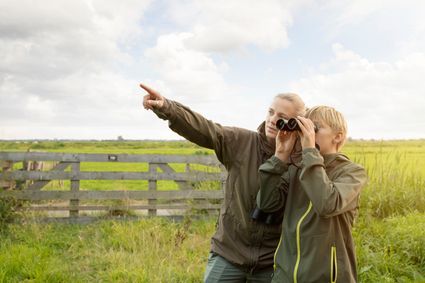 wijzende moeder die kind door de verrekijker laat zien wat er in het weiland is.