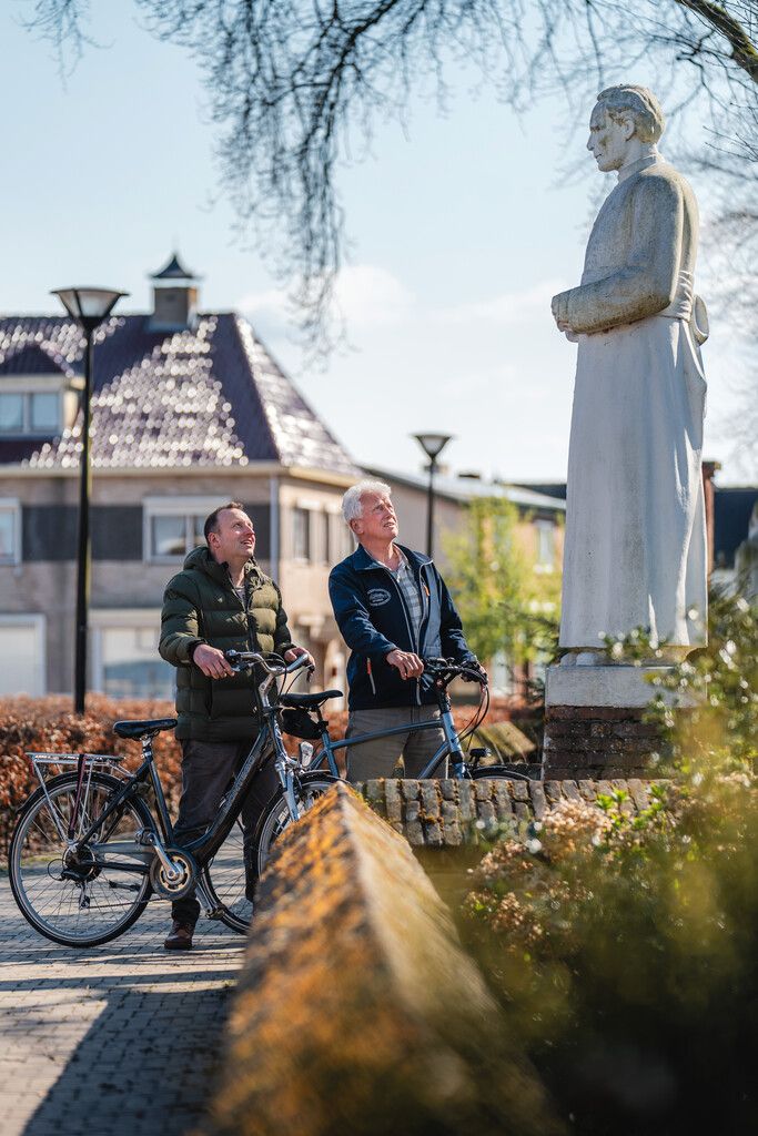 Twee fietsers kijken naar het monument van Pastoor Bastiaansen