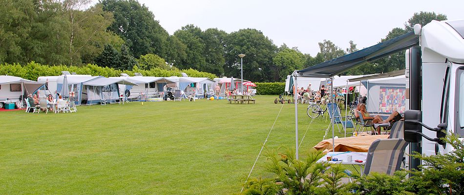 Een groen veld met rondom een groene rand van struiken en bomen en in het midden diverse caravans.