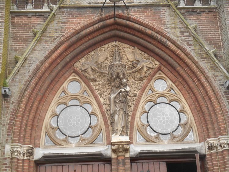 Een gotische boog van steen met Maria en kind. Links en rechts kleine roos venstertjes