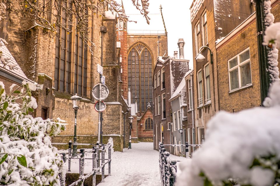 Een verstild wintermoment in het historische centrum: een smal straatje bedekt met een zachte laag sneeuw, omringd door oude gevels en de imposante kerk op de achtergrond. De besneeuwde daken, lantaarns en takken zorgen voor een warme, bijna sprookjesachtige sfeer waarin de geschiedenis van de stad voelbaar is.