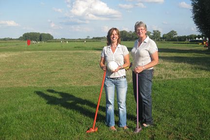 Twee personen staan met golfclubs in hun handen in een weiland.
