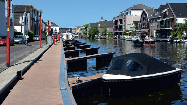 Aanlegplaatsen voor boten langs de Rijnkadehaven in Bodegraven, met moderne woningen, wandelaars en pleziervaart op een zonnige dag in het Groene Hart.
