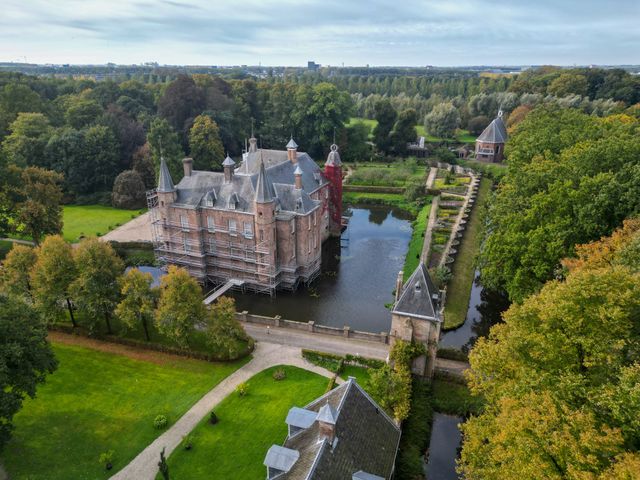 Een dronefoto van Slot Zuylen en haar tuinen met rode klimop die de toren van het slot beklimt