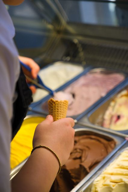 IJssalon De IJsscheppers in Oudewater, Groene Hart, detail van medewerker die een ijsje schept uit een vitrine met ambachtelijk schepijs in verschillende smaken zoals chocolade en fruitijs.