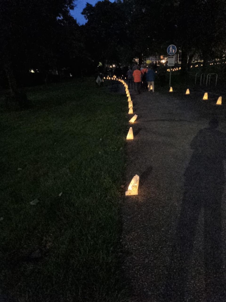 Deelnemers wandelen over een verlicht parkpad tijdens de 24 Uur van Woerden, met lichtzakken langs de route en een sfeervolle avondsetting in het groen.
