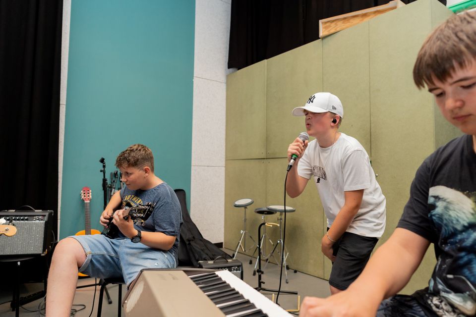 Muziekschool Muziekhuis in Oudewater, Groene Hart, bandcoaching met jongeren die samen muziek maken met zang, elektrische gitaar en keyboard in een repetitieruimte.