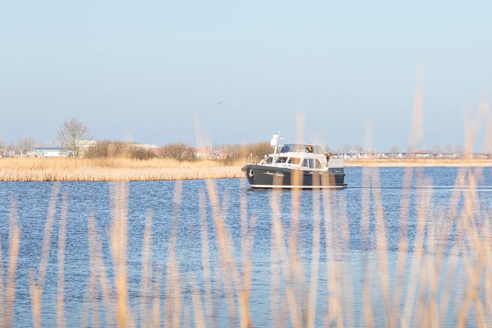 Een schip vaart een van de Friese meren in de winter, je ziet het schip uit focus achter een goudbruine rietkraag.