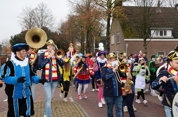 Foto met muzikanten, pieten en Sinterklaas op zijn paard in een vrolijke optocht.