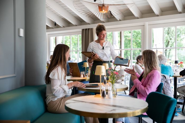 Twee dames binnen bij Restaurant ’t Ryck in Woerden krijgen de menukaart van een vriendelijke serveerster – (h)eerlijk tafelen in een warme, streekgebonden sfeer.
