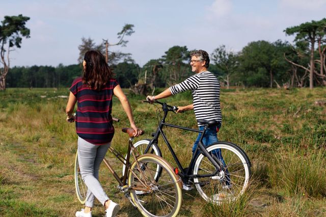 Ein Mann und eine Frau schieben ihre Fahrräder durch die Natur in Drenthe.