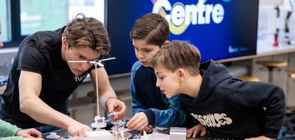 Twee jongens aan het kijken naar het werk van een medewerker in de Techniek studio van het science centre Delft