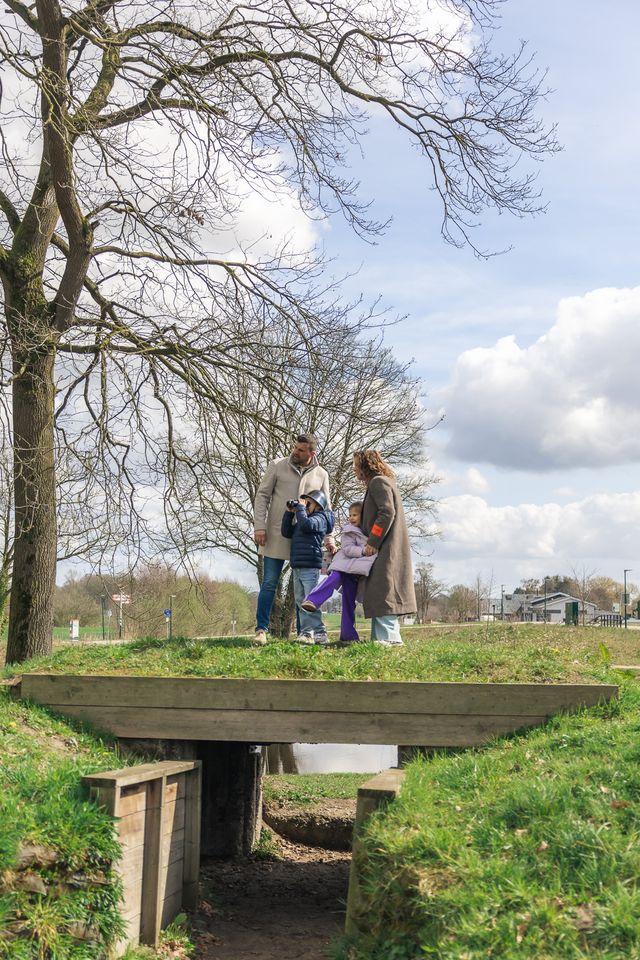 Kinderen met ouders bij Grebbelinie Bezoekerscentrum bij Fort aan de Buursteeg. Ze wijzen en kijken door een verrekijker.