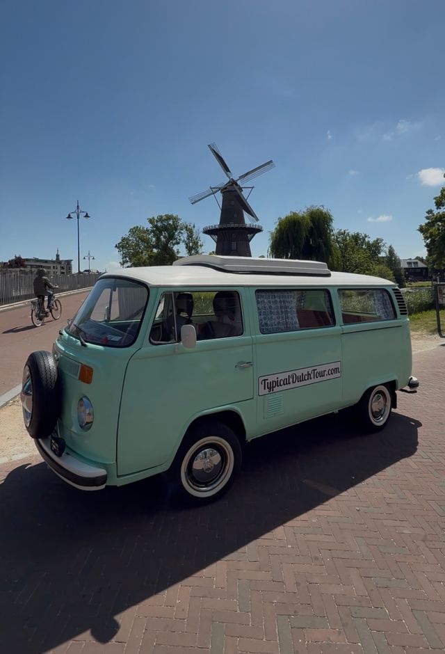 De zijkant van de tourbus van Typical Dutch Tour te zien in de stad met een molen op de achtergrond