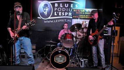 Bluesband treedt live op bij Bluespodium L’Esprit in Grand Café Zuidlaren, met gitarist, drummer en bassist op het podium – sfeervolle muziekavond in het Groene Hart.