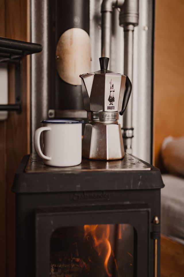 Bovenop een houtkachel staan een percolator en mok.