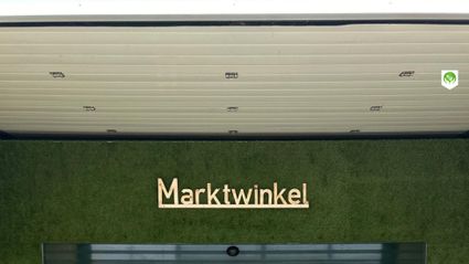 Streekwinkel De Marktwinkel in Woerden, Groene Hart, entree met glazen schuifdeuren en gevel met groen wandpaneel, binnen zichtbaar verse groenten, fruit en lokale producten in de verswinkel.