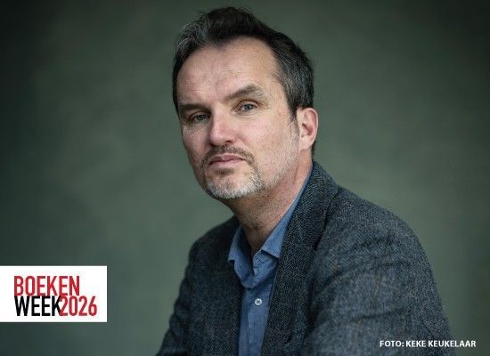 Portret van een volwassen man met korte donkere haren en lichte stoppelbaard, gekleed in een colbert en overhemd. Hij kijkt rustig en serieus in de camera. Linksonder staat het logo “Boekenweek 2026”, rechtsonder een fotocredit.