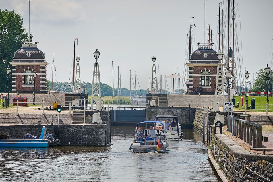 Twee boten varen in de sluis van Lemmer. Op de achtergrond staan masten van zeilboten.