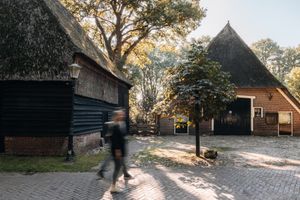 Een man en een vrouw wandelen langs een authentieke Saksische boerderij in een Drents brinkdorpje.